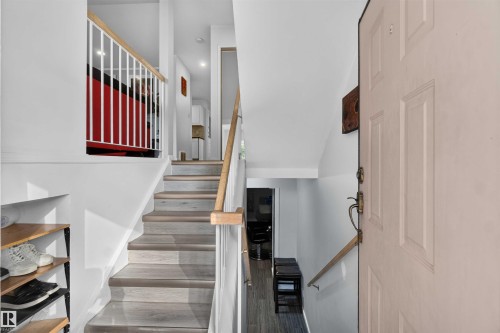 Wood-finish flooring on stairs, white baluster railing, natural wood handrails, and a paneled entry door with brass hardware - #28 3645 145 Av Nw, Edmonton, AB - Indoor Photo Showing Other Room