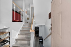 Wood-finish flooring on stairs, white baluster railing, natural wood handrails, and a paneled entry door with brass hardware - 