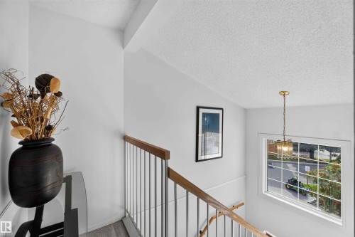 Stairwell featuring a wood handrail, metal balusters, and a window with natural light - #28 3645 145 Av Nw, Edmonton, AB - Indoor Photo Showing Other Room