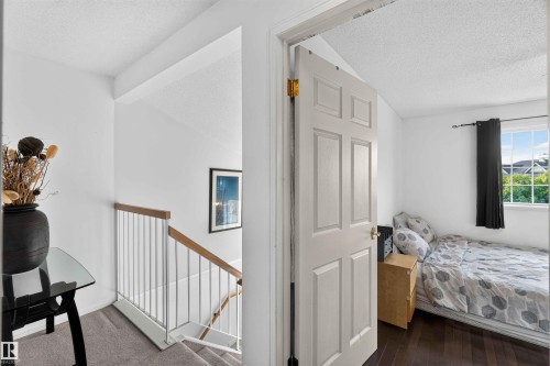 Hardwood flooring, window with exterior scenery, white wall finishes, paneled door, and carpeted stairs with a wood and metal railing - #28 3645 145 Av Nw, Edmonton, AB - Indoor Photo Showing Bedroom