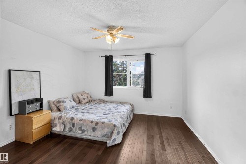 Hardwood flooring, white walls, ceiling fan with integrated lighting, and a window with black curtains - #28 3645 145 Av Nw, Edmonton, AB - Indoor Photo Showing Bedroom