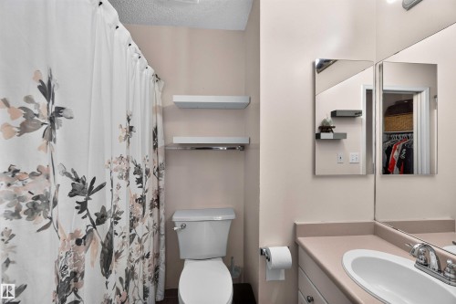 Bathroom featuring a toilet, built-in vanity with a single sink, wall-mounted mirror, and floating shelving - #28 3645 145 Av Nw, Edmonton, AB - Indoor Photo Showing Bathroom