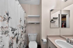 Bathroom featuring a toilet, built-in vanity with a single sink, wall-mounted mirror, and floating shelving - 