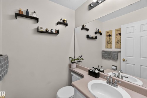 Bathroom featuring a vanity with an integrated sink, a large wall-mounted mirror, and a two-panel interior door - #28 3645 145 Av Nw, Edmonton, AB - Indoor Photo Showing Bathroom