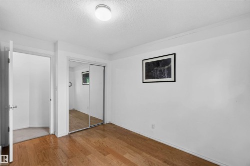 Hardwood flooring, mirrored closet doors, ceiling-mounted light fixture, and white wall finishes - #28 3645 145 Av Nw, Edmonton, AB - Indoor Photo Showing Other Room