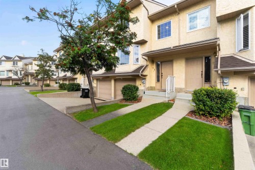 Multi-level stucco exterior with multiple windows, private entrance, attached garage, and landscaped front yard with a paved driveway - #28 3645 145 Av Nw, Edmonton, AB - Outdoor With Facade