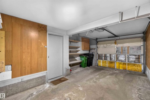 Concrete flooring garage with an overhead door, wood paneling, built-in shelving, and a service door - #28 3645 145 Av Nw, Edmonton, AB - Indoor Photo Showing Garage
