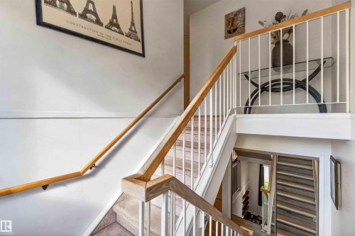 Multi-level staircase featuring a wood-finish handrail, white balusters, and carpeted treads - #28 3645 145 Av Nw, Edmonton, AB - Indoor Photo Showing Other Room
