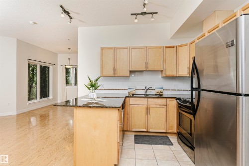 Kitchen featuring wood cabinetry, stainless steel appliances, and a dark stone countertop island - #219 10333 112 St Nw, Edmonton, AB - Indoor Photo Showing Kitchen With Double Sink