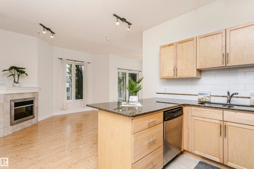 Kitchen featuring granite countertops, wood-finish cabinetry, a stainless steel dishwasher, and a subway tile backsplash - #219 10333 112 St Nw, Edmonton, AB - Indoor Photo Showing Kitchen With Fireplace With Double Sink