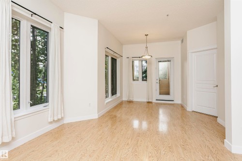Wood-finish flooring, multiple large windows, pendant light fixture, white paneled doors, and a glass-paned exterior door - #219 10333 112 St Nw, Edmonton, AB - Indoor Photo Showing Other Room