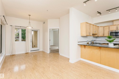 Light wood-finish flooring, kitchen featuring light wood cabinetry, dark countertops, white subway tile backsplash, and stainless steel appliances - #219 10333 112 St Nw, Edmonton, AB - Indoor Photo Showing Kitchen