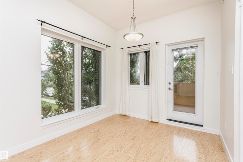 Wood-finish flooring, white walls, multiple windows, glass-paneled door, and a suspended ceiling light fixture - #219 10333 112 St Nw, Edmonton, AB - Indoor Photo Showing Other Room