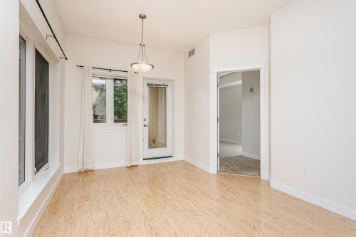 Wood-finish flooring, multiple windows, a glass-paned door, and a suspended lighting fixture - #219 10333 112 St Nw, Edmonton, AB - Indoor Photo Showing Other Room