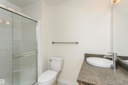 Glass-enclosed shower with white tiled surround, toilet, vanity with integrated basin, polished chrome faucet, and mirrored wall - 