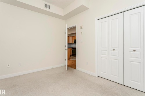 Carpeted flooring, white walls, and bifold closet doors with silver hardware - #219 10333 112 St Nw, Edmonton, AB - Indoor Photo Showing Other Room