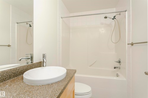Bathroom featuring a vanity with a white vessel sink, a speckled countertop, and a shower-tub combination with a white surround - #219 10333 112 St Nw, Edmonton, AB - Indoor Photo Showing Bathroom