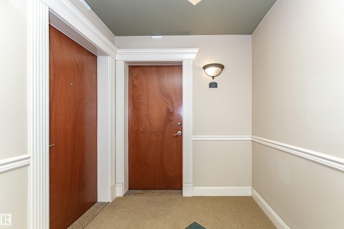 Entryway with wood-finish doors, detailed white trim, and a decorative wall sconce - #219 10333 112 St Nw, Edmonton, AB - Indoor Photo Showing Other Room