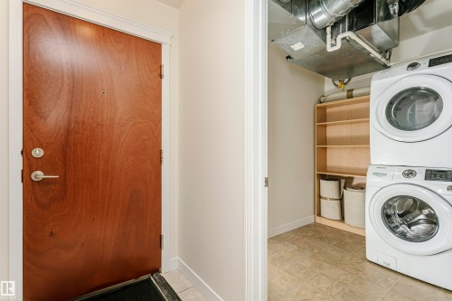 Laundry area with stacked washing machine and dryer, built-in shelving, and tiled flooring - #219 10333 112 St Nw, Edmonton, AB - Indoor Photo Showing Laundry Room