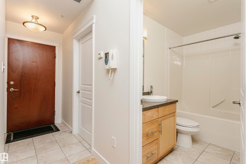Tile flooring, wood-finish entry door, ceiling-mounted light fixture, bathroom vanity with surface-mount sink, and shower-tub combination - #219 10333 112 St Nw, Edmonton, AB - Indoor Photo Showing Bathroom