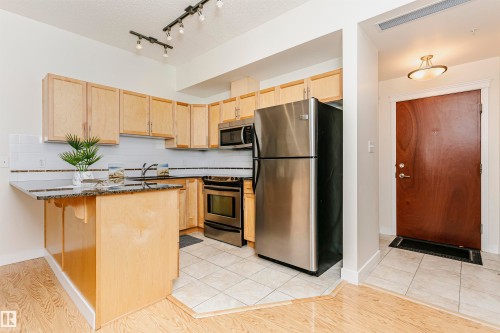 Kitchen featuring stainless steel appliances, light wood-finish cabinetry, and a granite-look countertop island - #219 10333 112 St Nw, Edmonton, AB - Indoor Photo Showing Kitchen