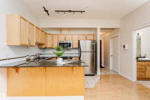 Kitchen featuring light wood cabinetry, dark speckled countertops, stainless steel appliances, and a white tile backsplash - #219 10333 112 St Nw, Edmonton, AB - Indoor Photo Showing Kitchen