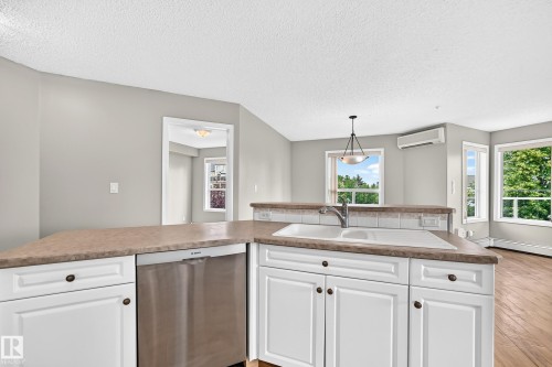 Kitchen featuring white cabinetry, a built-in stainless steel dishwasher, a white sink with a chrome faucet, and a stone-look countertop - #331 9704 174 St Nw, Edmonton, AB 