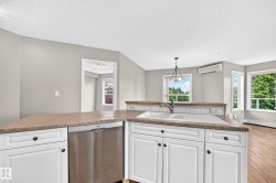 Kitchen featuring white cabinetry, a built-in stainless steel dishwasher, a white sink with a chrome faucet, and a stone-look countertop - 