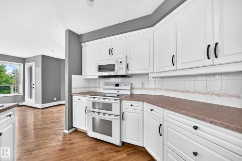 Kitchen featuring white cabinetry, integrated microwave, double oven, and wood-finish flooring - #331 9704 174 St Nw, Edmonton, AB 