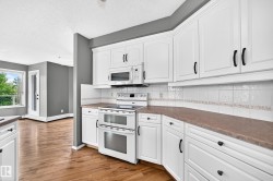 Kitchen featuring white cabinetry, integrated microwave, double oven, and wood-finish flooring - 