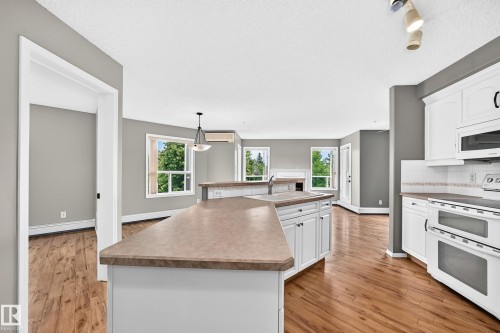 Kitchen featuring white cabinetry, a built-in microwave, a double oven range, a kitchen island with a sink, and wood-finish flooring - #331 9704 174 St Nw, Edmonton, AB 