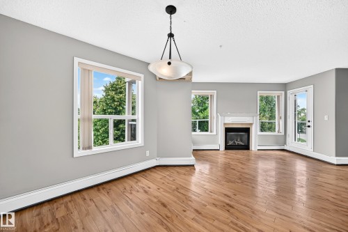 Wood-finish flooring, multiple windows, a decorative fireplace with a mantel, a glass-paned exterior door, and an overhead light fixture - #331 9704 174 St Nw, Edmonton, AB 