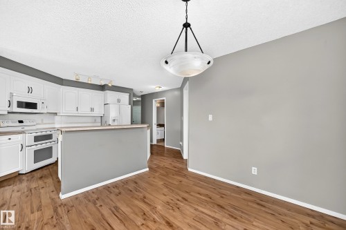 Wood-finish flooring, white cabinetry, integrated kitchen appliances, a breakfast bar, and a hanging light fixture - #331 9704 174 St Nw, Edmonton, AB 