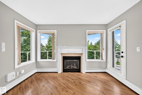 Wood-finish flooring with a white trim fireplace and three distinct windows - #331 9704 174 St Nw, Edmonton, AB 