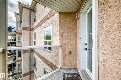 Balcony with glass railing, textured exterior finish, and a white framed door - #331 9704 174 St Nw, Edmonton, AB 