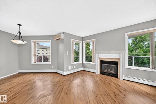 Recessed fireplace with a decorative mantel, wood-finish flooring, multiple windows, and a ceiling-mounted light fixture - #331 9704 174 St Nw, Edmonton, AB 