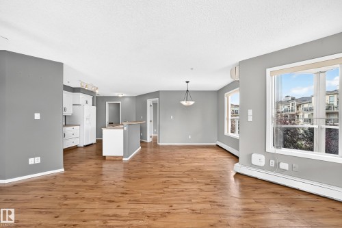 Wood-finish flooring throughout, white kitchen cabinetry with contemporary hardware, and a center island - #331 9704 174 St Nw, Edmonton, AB 