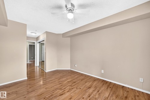 Spacious room featuring wood-finish flooring, a ceiling fan with integrated lighting, and mirrored closet doors - #331 9704 174 St Nw, Edmonton, AB 