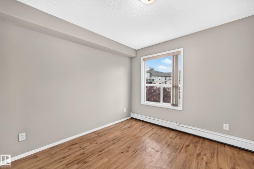 Wood-finish flooring, neutral wall paint, and a large window providing natural light - #331 9704 174 St Nw, Edmonton, AB 