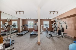 Fitness area featuring resilient flooring, track lighting, multiple windows, and a full-wall mirror - 