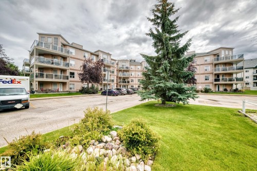 Multi-story building with multiple balconies featuring glass railings, light-colored exterior siding, and a sloped roofline - #331 9704 174 St Nw, Edmonton, AB 