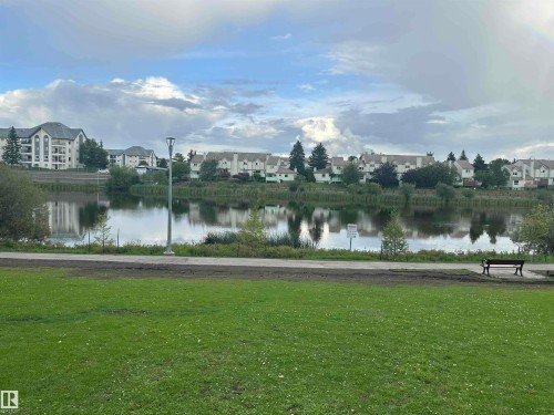 Expansive green space featuring a paved pathway, mature trees, and a tranquil pond - #331 9704 174 St Nw, Edmonton, AB 