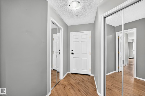 Hallway featuring wood-finish flooring, two mirrored closet doors, a paneled entry door, and recessed lighting - #331 9704 174 St Nw, Edmonton, AB 