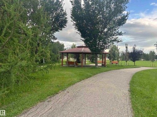 Paved walking path winding through a park setting with a covered gazebo featuring built-in benches - #331 9704 174 St Nw, Edmonton, AB 