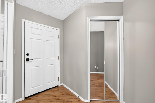 Entryway featuring wood-finish flooring, a white paneled door with matte black hardware, and a closet with mirrored sliding doors - #331 9704 174 St Nw, Edmonton, AB 