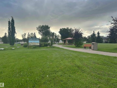 Expansive green space featuring a paved walking path, mature trees, a park sign, and a built-in gazebo - #331 9704 174 St Nw, Edmonton, AB 