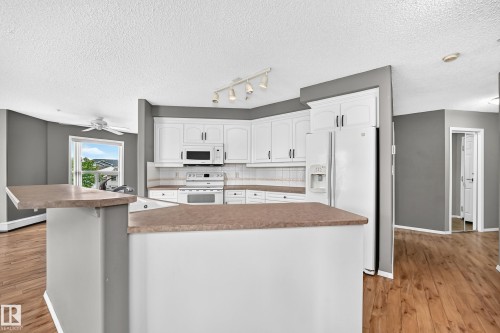 Kitchen featuring white cabinetry, white appliances, a tile backsplash, and a breakfast bar - #331 9704 174 St Nw, Edmonton, AB 