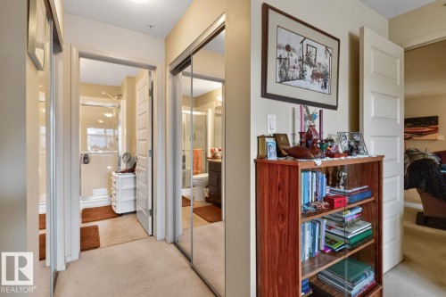 Mirrored closet doors, light-colored carpeting, and a visible doorway to a full bathroom with a glass-enclosed shower - #210 7909 71 St Nw, Edmonton, AB - Indoor Photo Showing Other Room