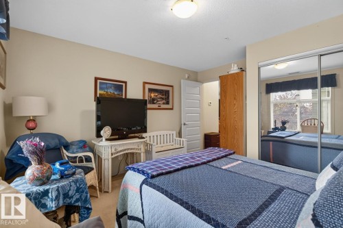 Mirrored closet doors, flush-mount ceiling light fixture, neutral wall color, white interior door, wood-finish cabinetry - #210 7909 71 St Nw, Edmonton, AB - Indoor Photo Showing Bedroom
