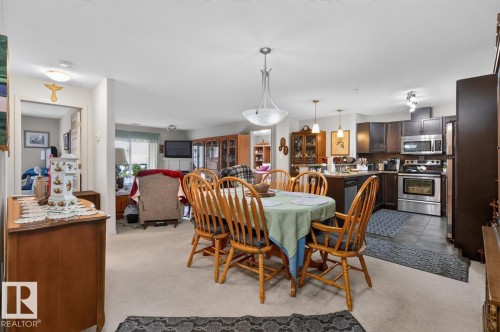 Open-concept living space featuring a dining area with a chandelier, a kitchen with dark wood-finish cabinetry, and stainless steel appliances - #210 7909 71 St Nw, Edmonton, AB - Indoor Photo Showing Dining Room